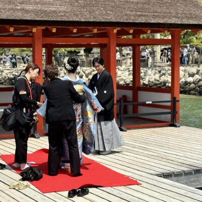 A woman in a blue kimono stands on a red carpet by a waterfront pavilion