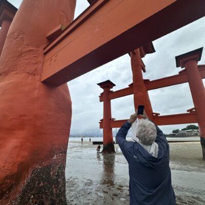 A person in a blue jacket takes a photo of the large red torii gate at Itsukushima Shrine, one of the best things to do in Japan,