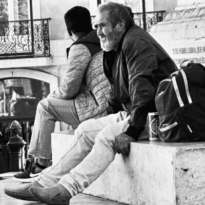 A grayscale photo shows two men sitting on a stone ledge, facing away from each other.